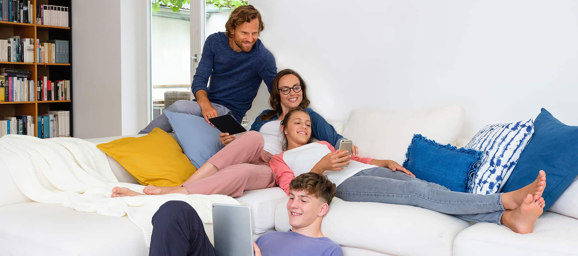 Mann, Frau, Mädchen und Junge liegen auf einer Couch und lesen auf eReadern.