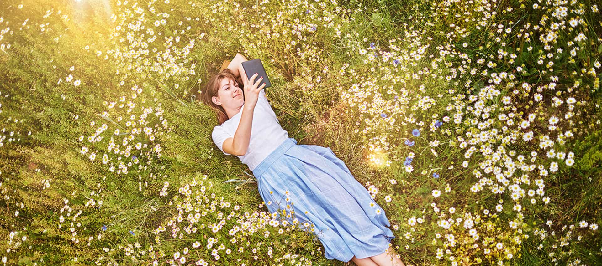 Mädchen auf Blumenwiese mit tolino-eReader in der Hand.