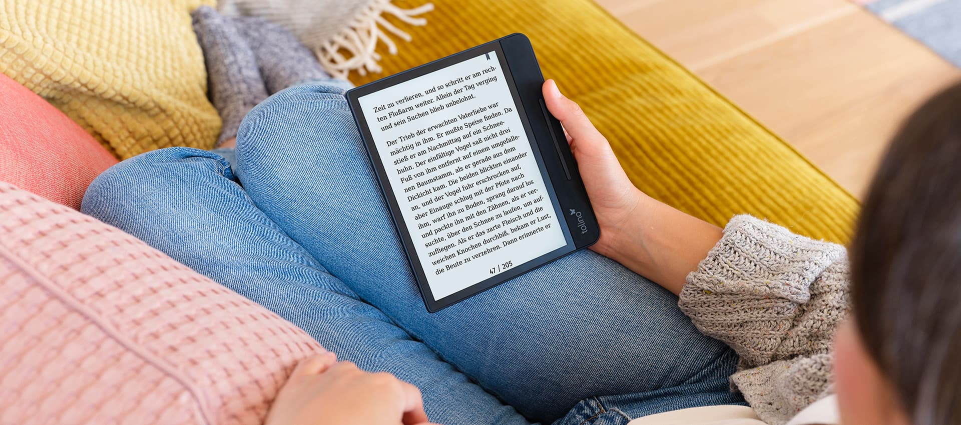 Frau liegt auf Couch und hält einen tolino-eReader, der den neuen Vergrößerungsmodus zeigt.